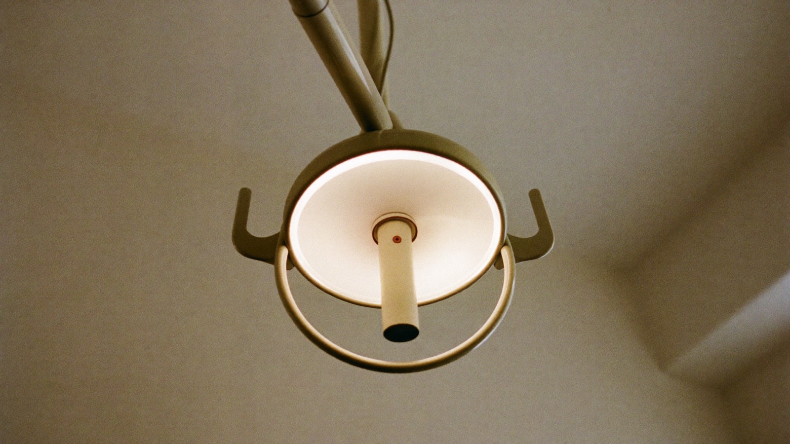 The round overhead operating light of a dental chair, seen from below, glowing against a plain ceiling.