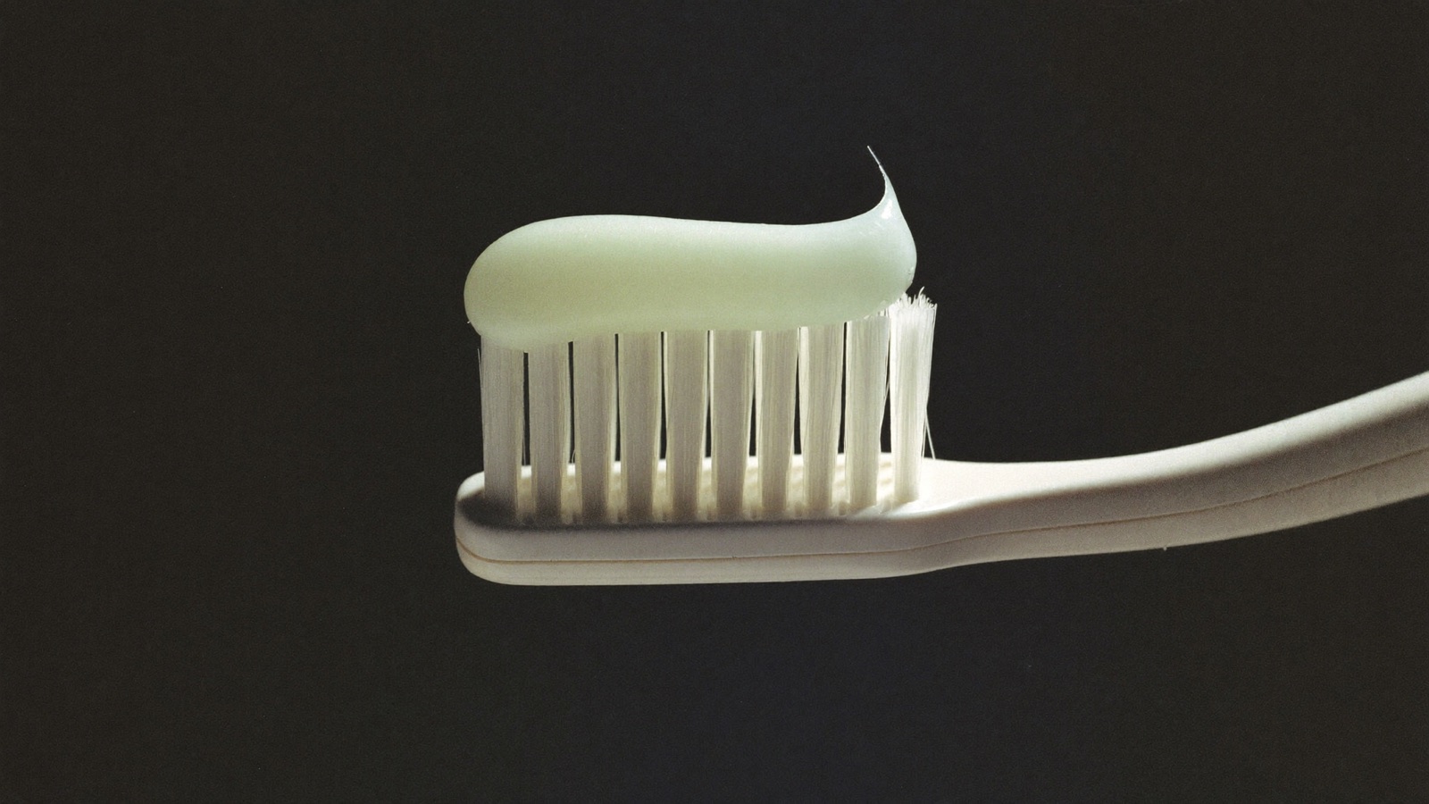 A close-up of a bead of toothpaste sitting on the bristles of a toothbrush against a dark background.